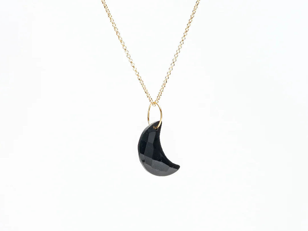 Gold chain necklace with a faceted black crescent moon pendant on a white background