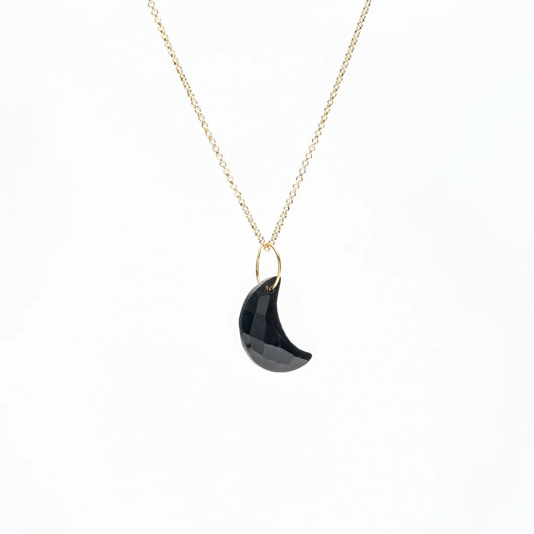 Gold chain necklace with a faceted black crescent moon pendant on a white background