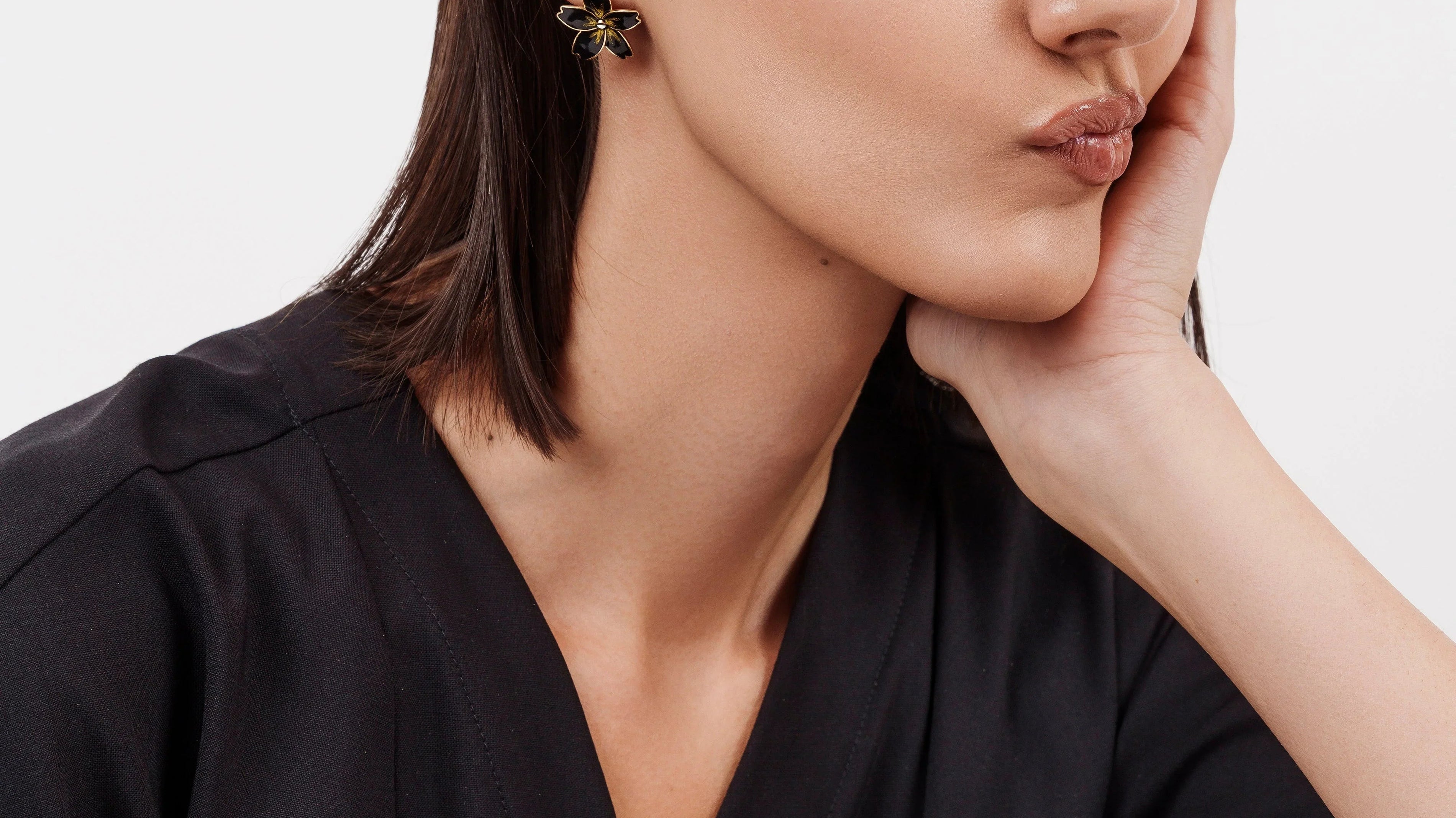 Woman with sleek dark hair wearing black outfit and flower-shaped black and gold earrings