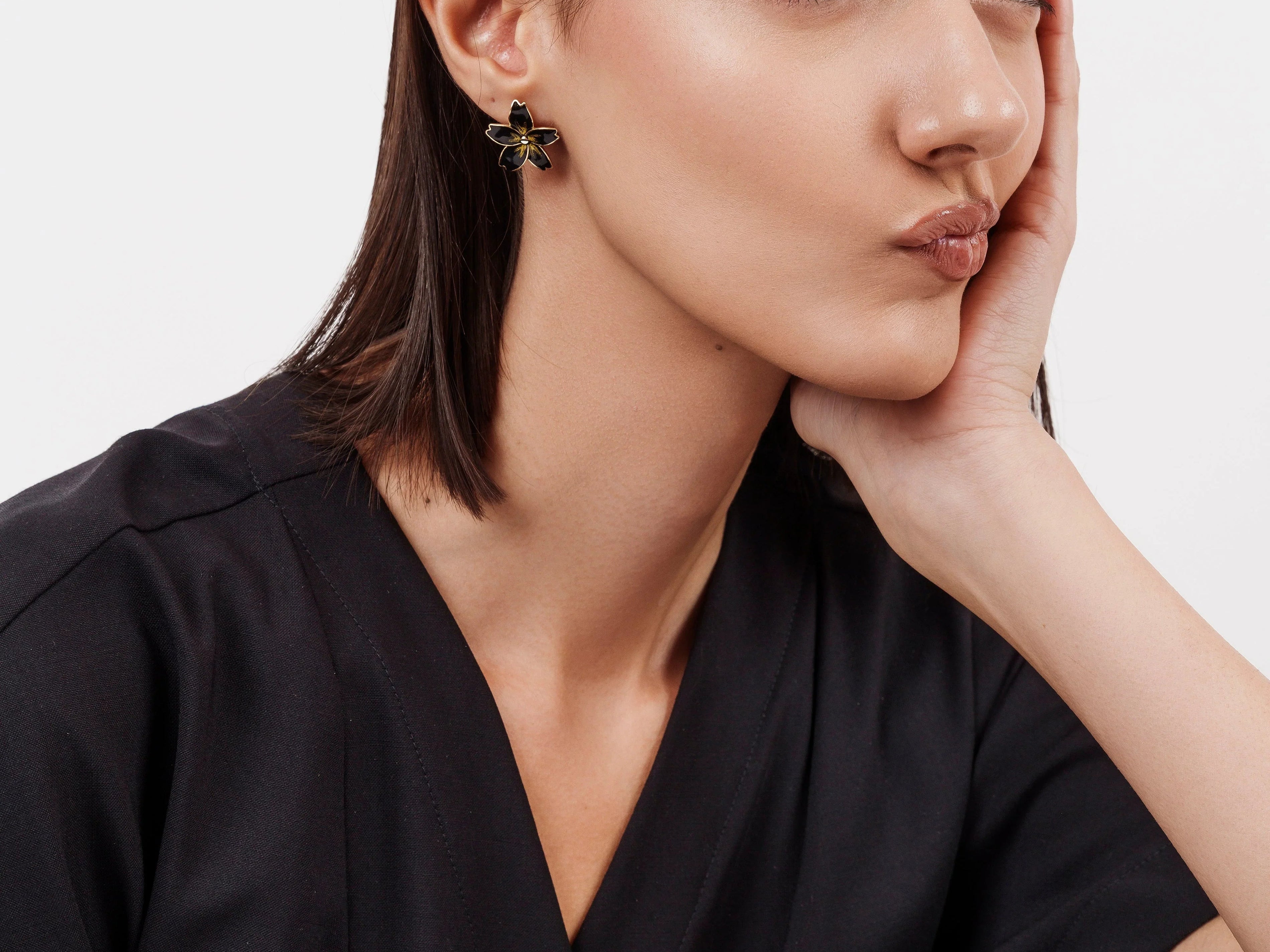 Woman with sleek dark hair wearing black outfit and flower-shaped black and gold earrings