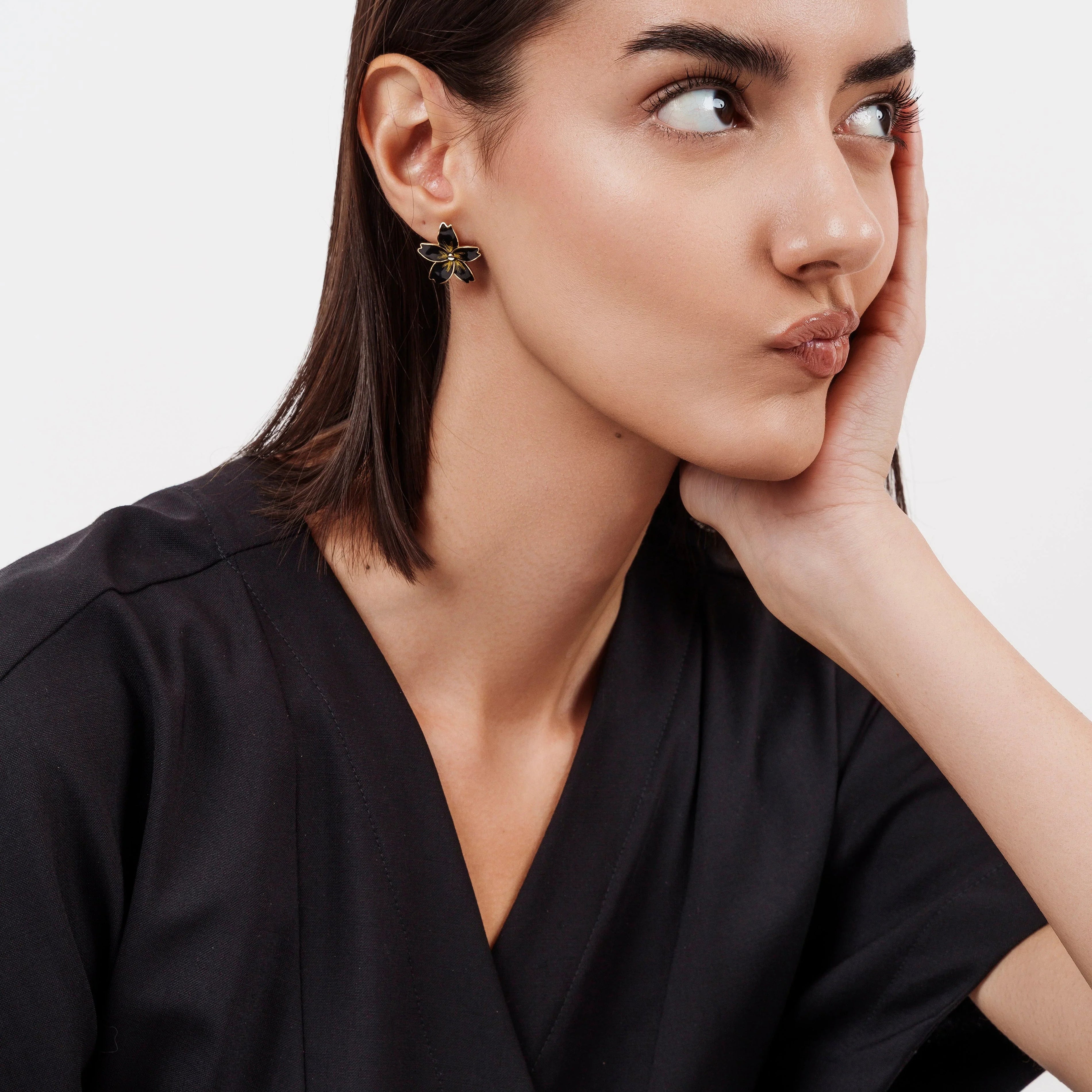 Woman with sleek dark hair wearing black outfit and flower-shaped black and gold earrings