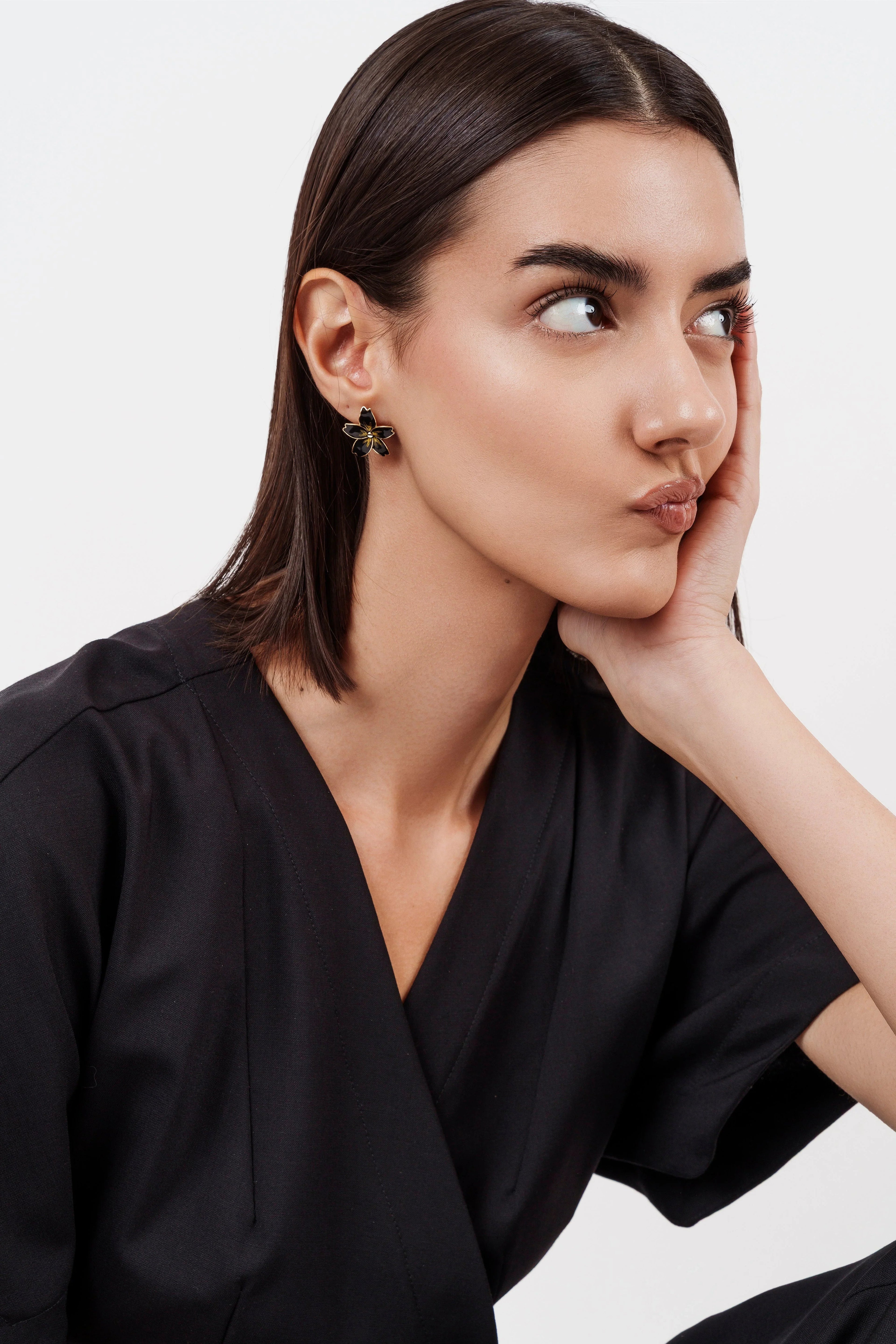 Woman with sleek dark hair wearing black outfit and flower-shaped black and gold earrings