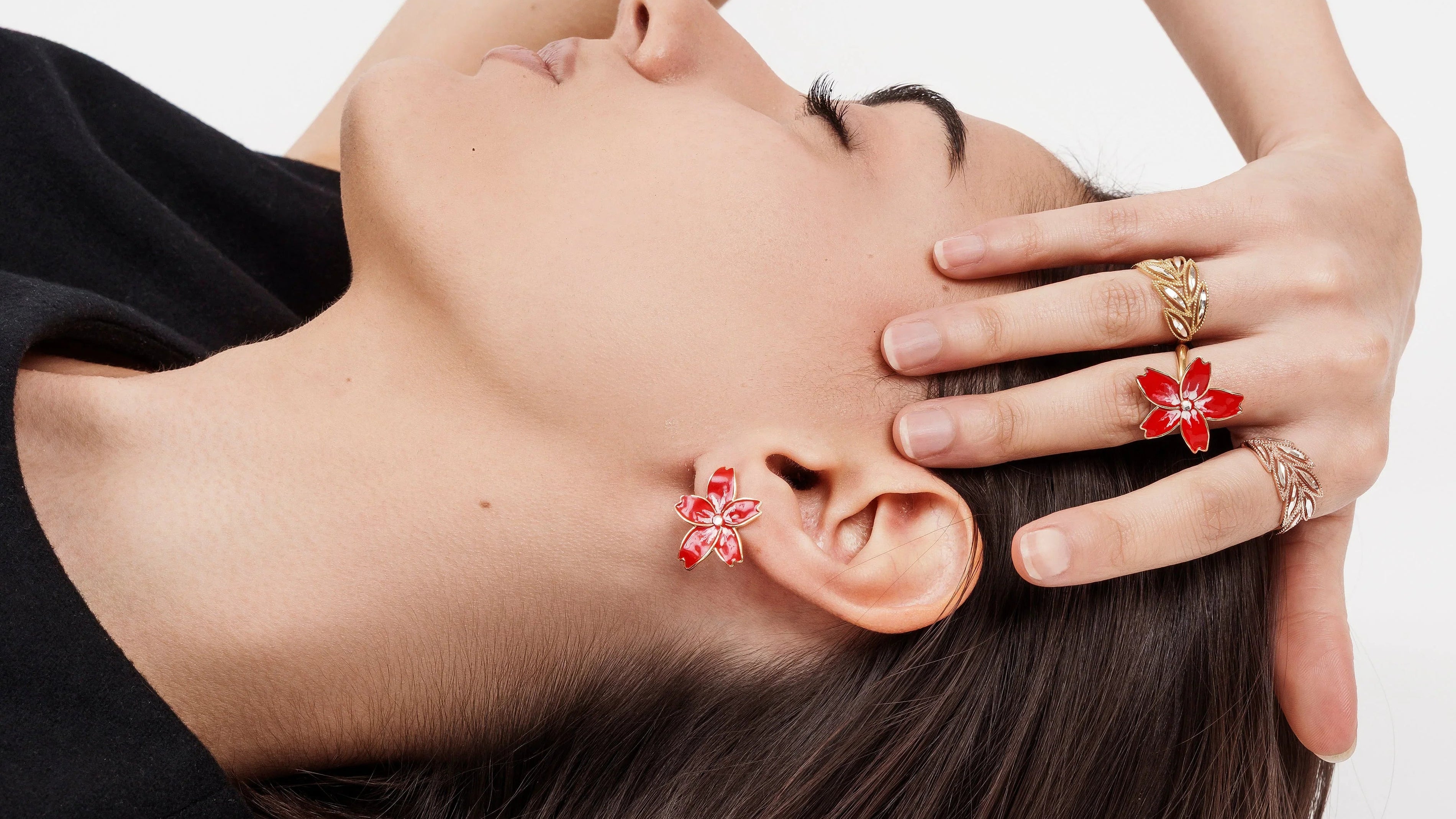 Close-up of woman lying down wearing red floral earrings and gold rings with red floral design