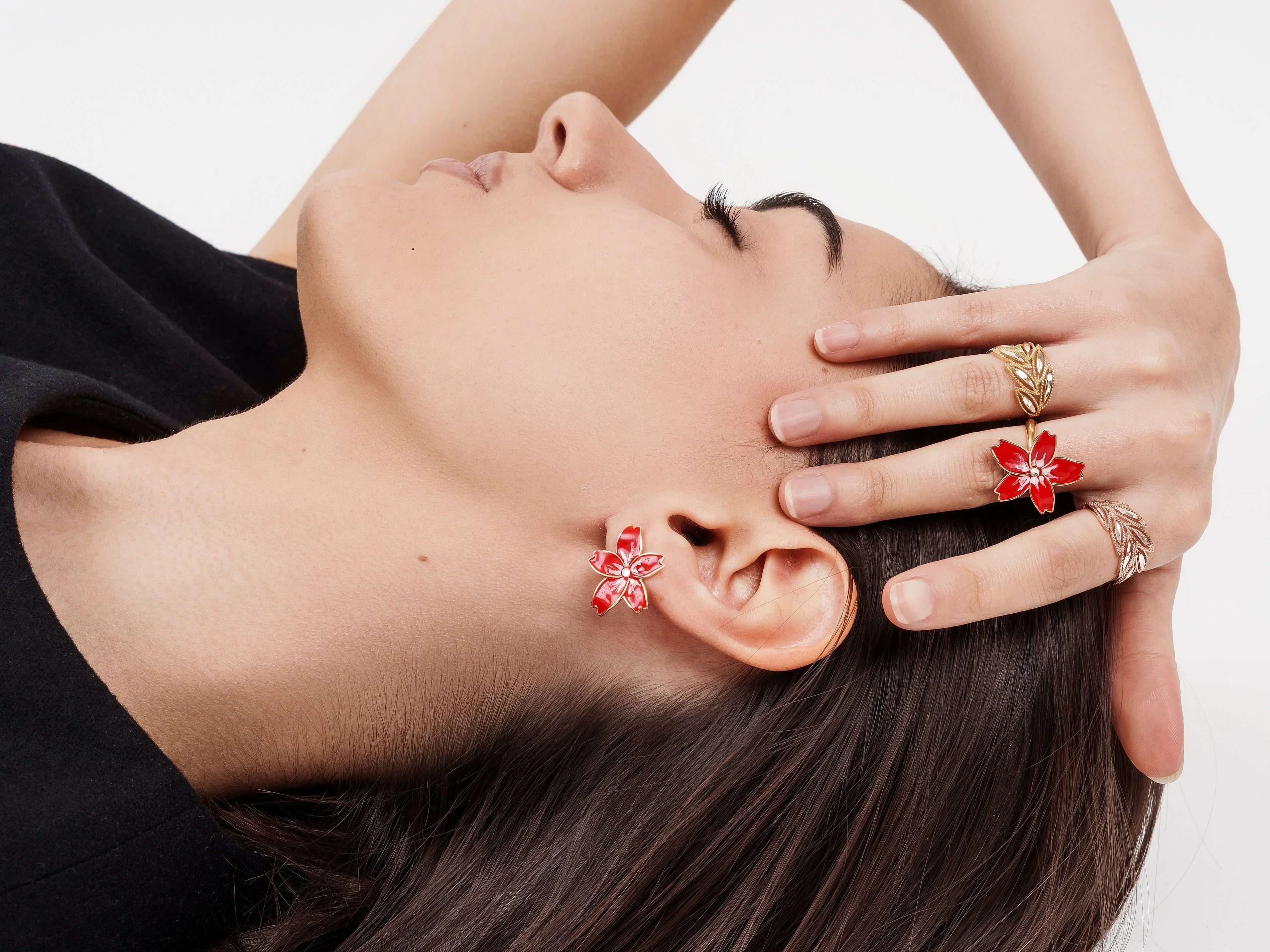 Close-up of woman lying down wearing red floral earrings and gold rings with red floral design