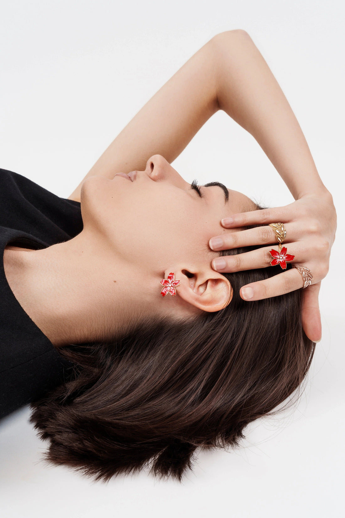 Close-up of woman lying down wearing red floral earrings and gold rings with red floral design