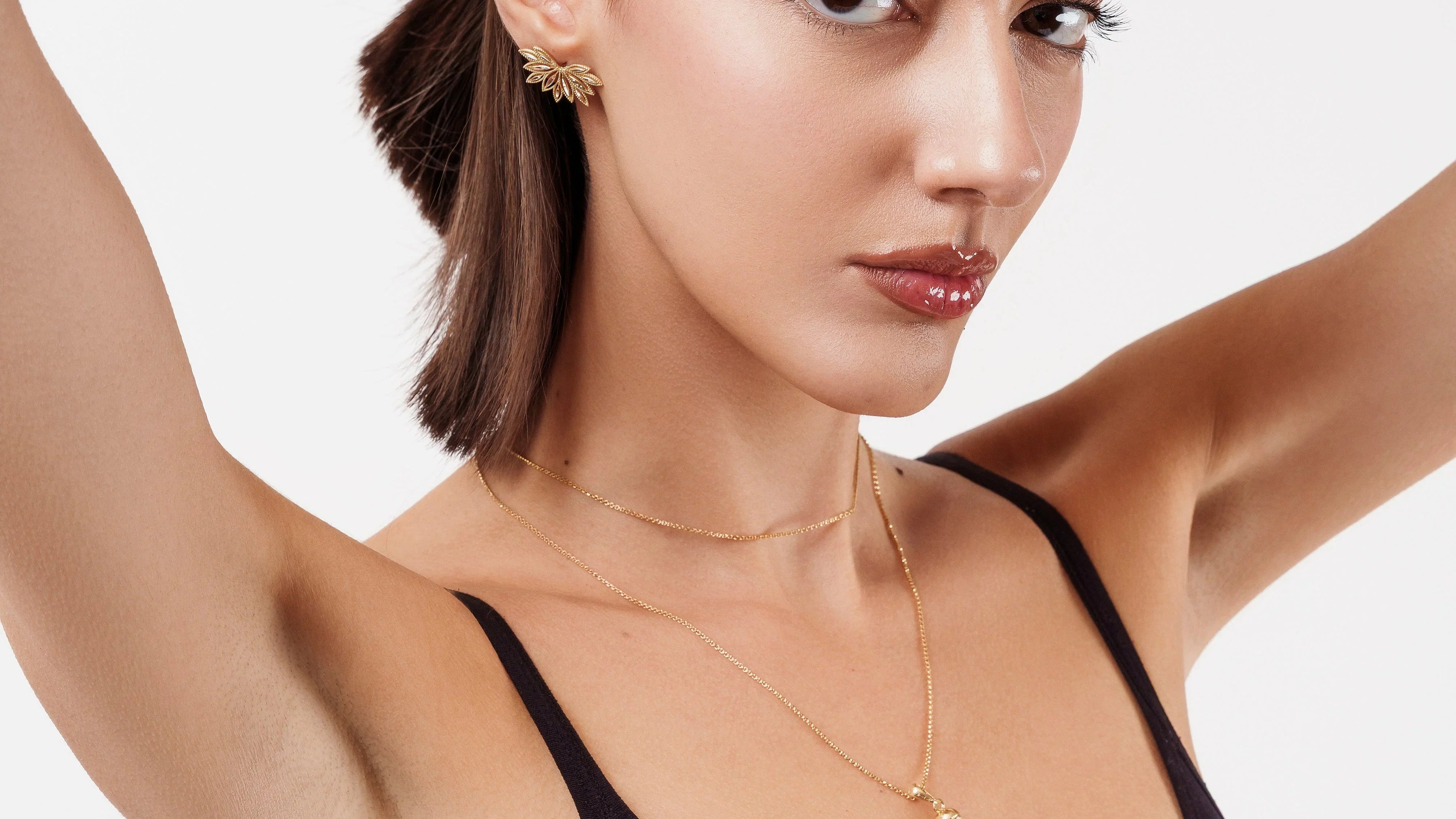 Woman in black tank top wearing gold leaf earrings and a gold pendant necklace against white background