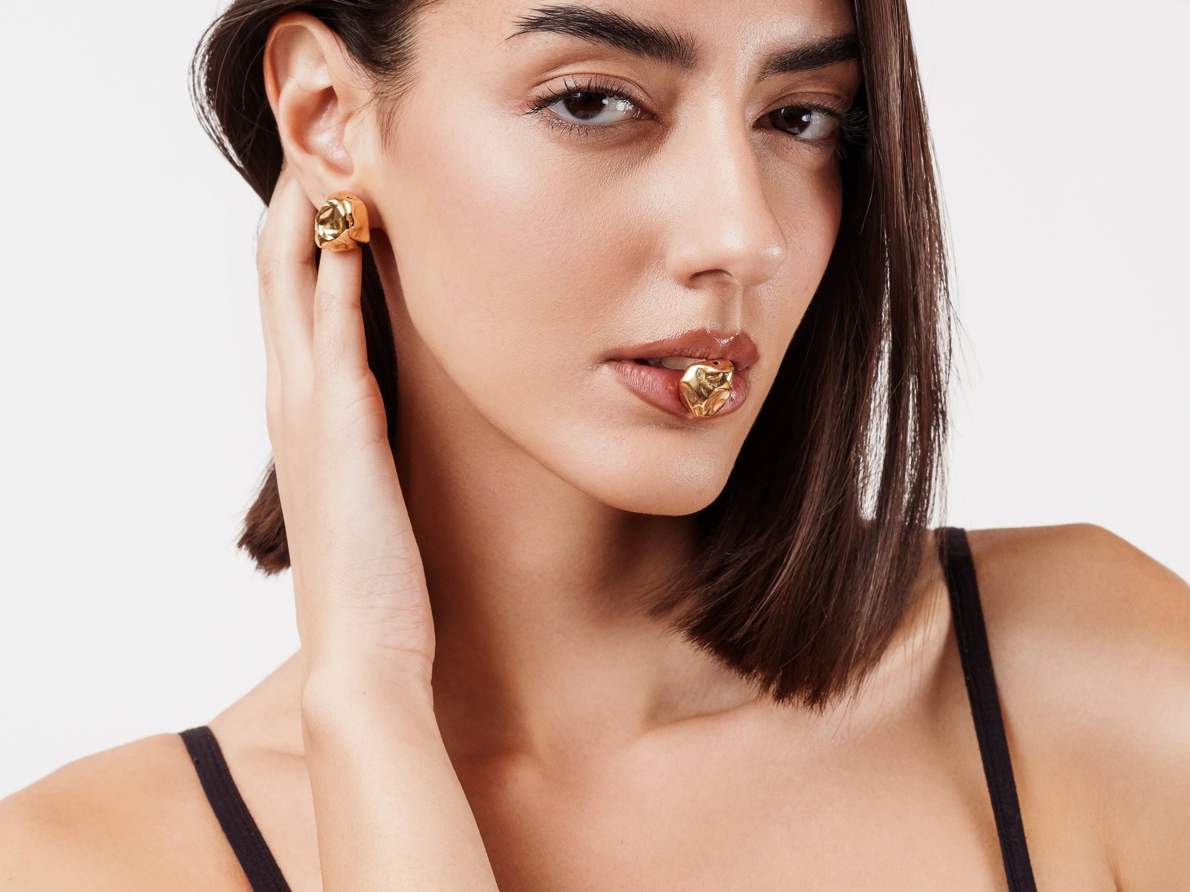 Close-up portrait of woman wearing black top and gold statement earrings with matching lip accessory