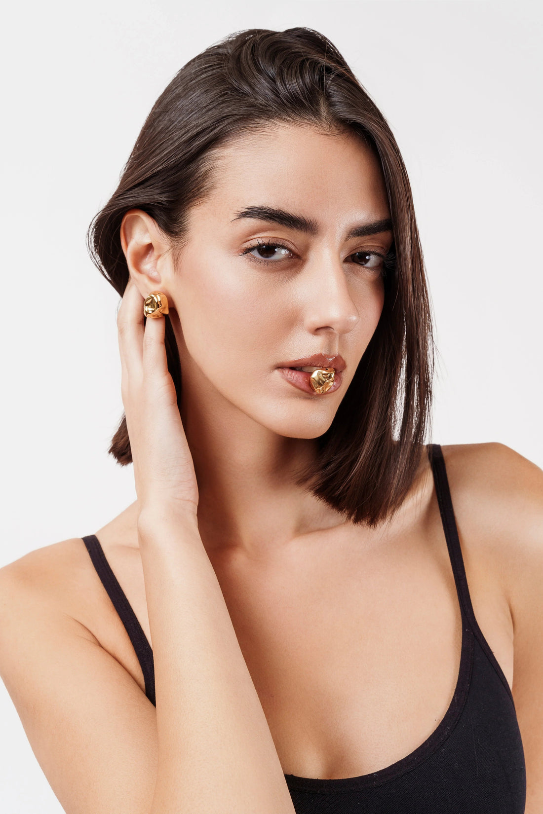 Close-up portrait of woman wearing black top and gold statement earrings with matching lip accessory