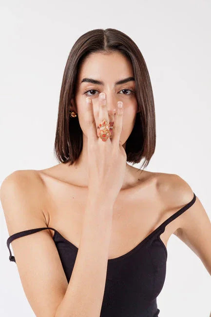 Woman with straight dark hair wearing black off-shoulder top and ornate red gold ring covering part of her face