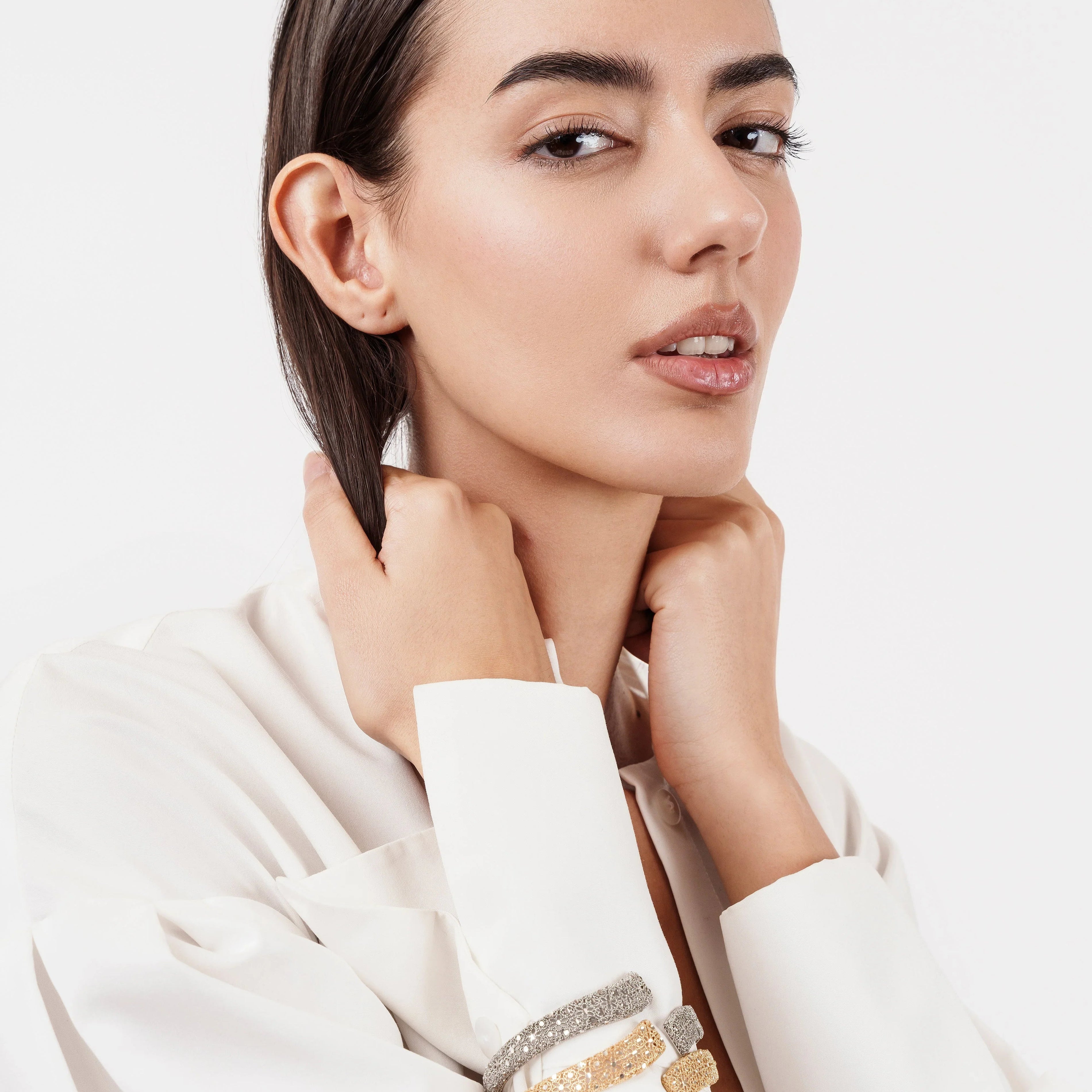 Fashion model in white blouse wearing gold and silver textured bracelets on wrist