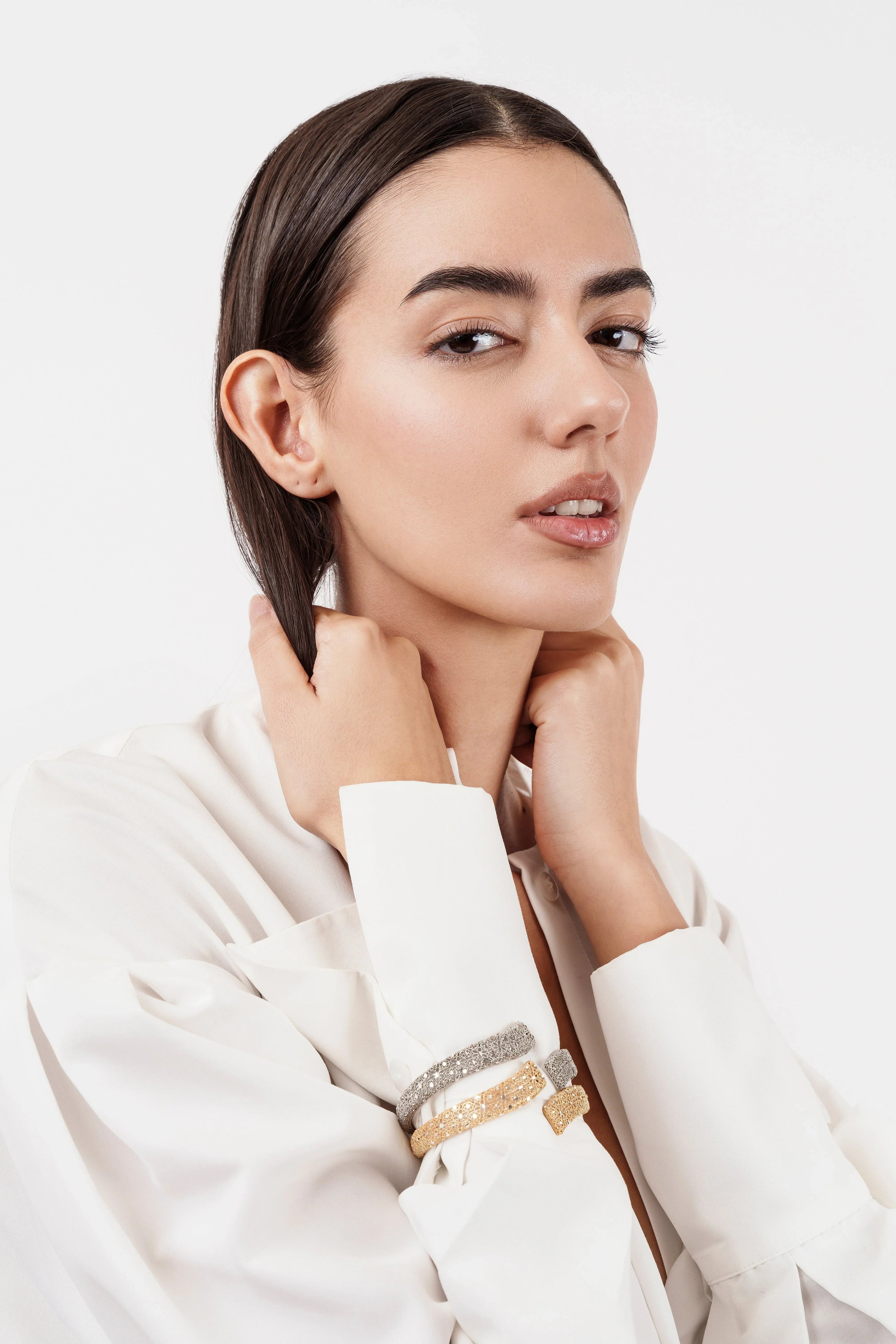 Fashion model in white blouse wearing gold and silver textured bracelets on wrist