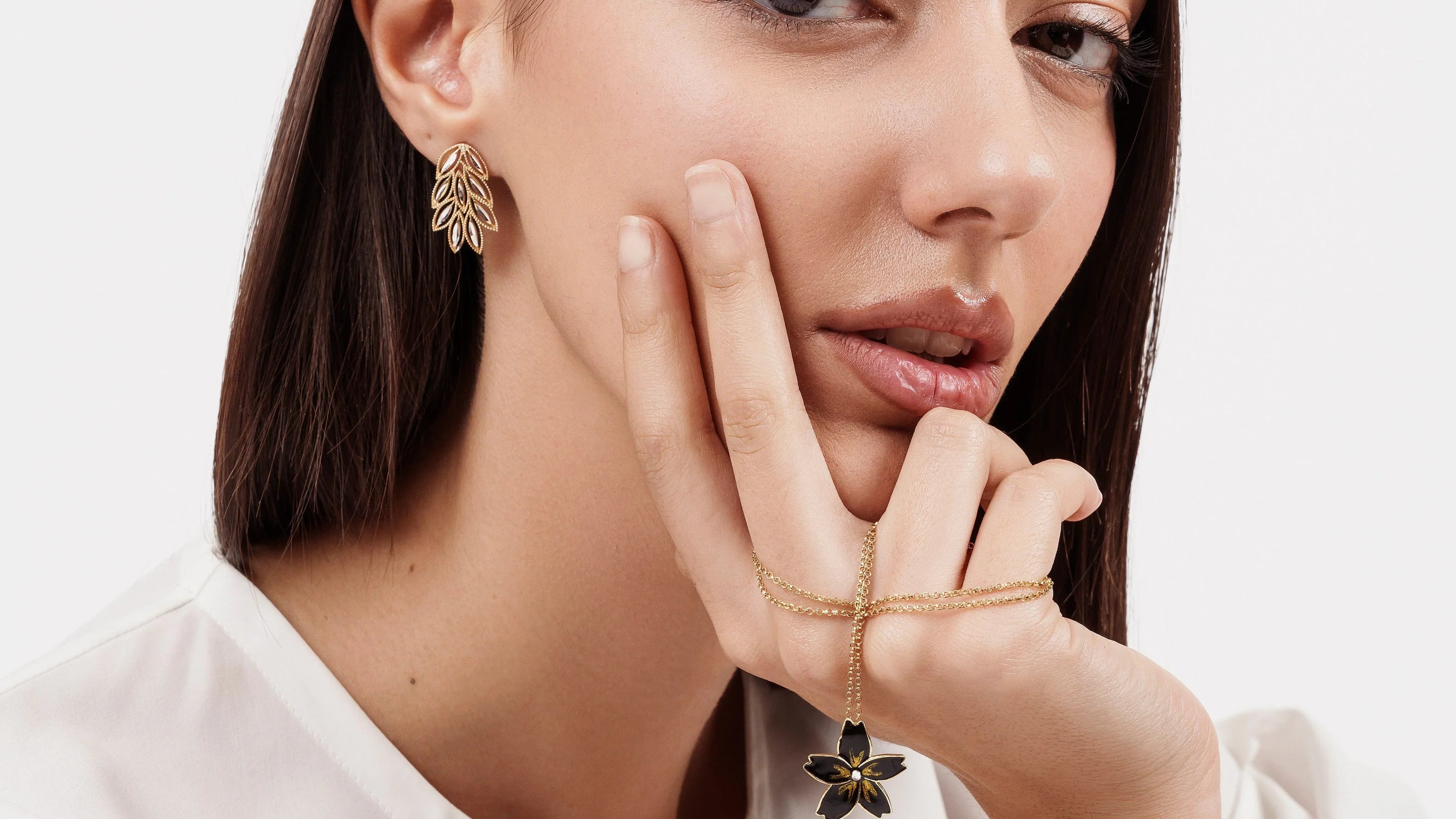 Close-up of woman with dark hair wearing gold leaf earrings and holding a gold flower pendant necklace