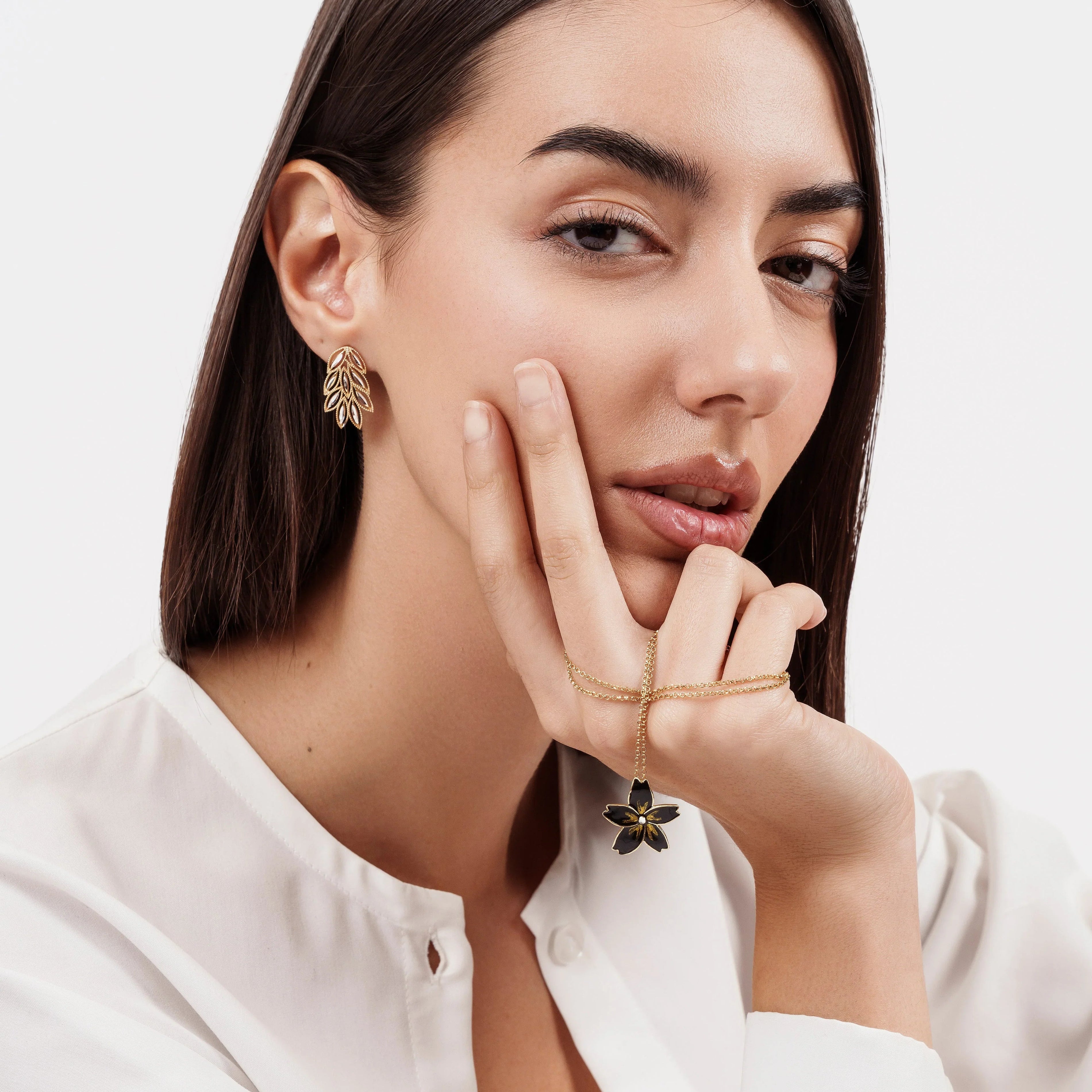 Close-up of woman with dark hair wearing gold leaf earrings and holding a gold flower pendant necklace