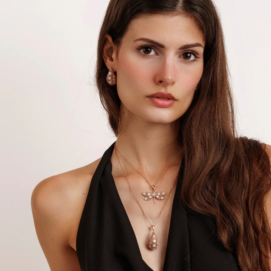 Woman wearing rose gold dragonfly and teardrop pendant necklaces and matching earrings with black halter top