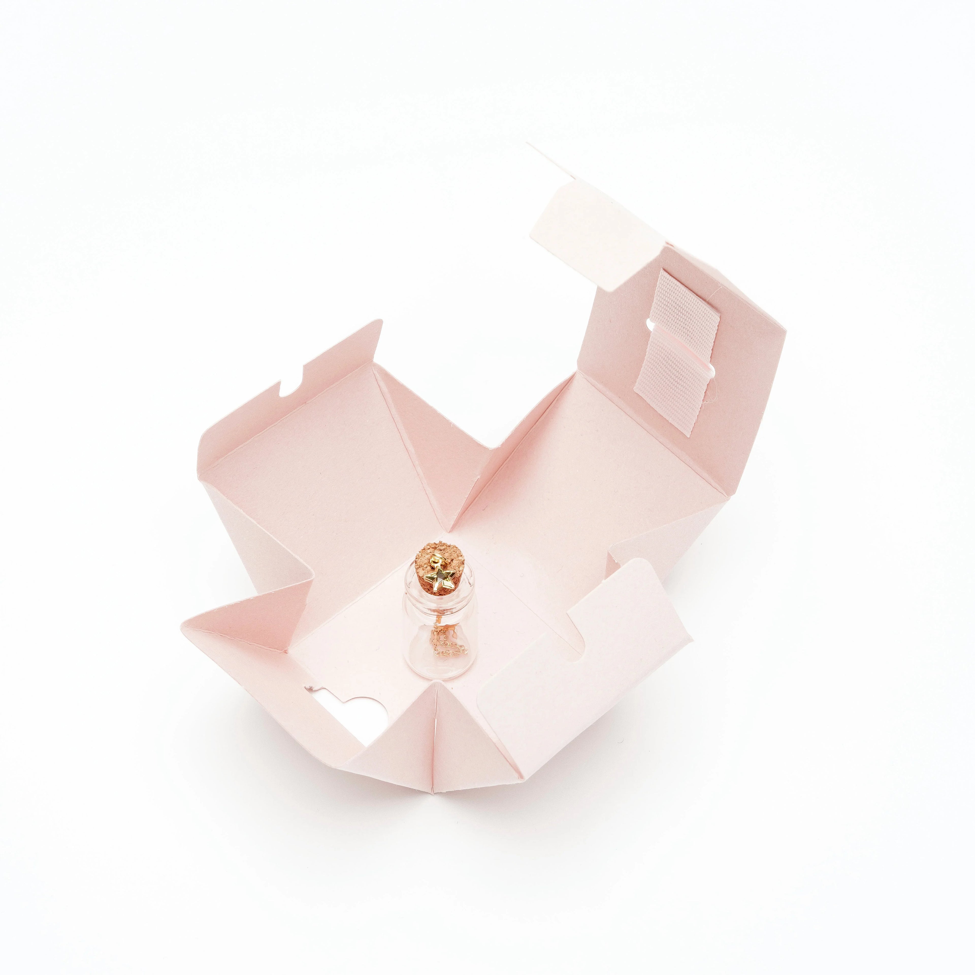 Small transparent glass bottle with cork and gold star charms inside pink foldable gift box