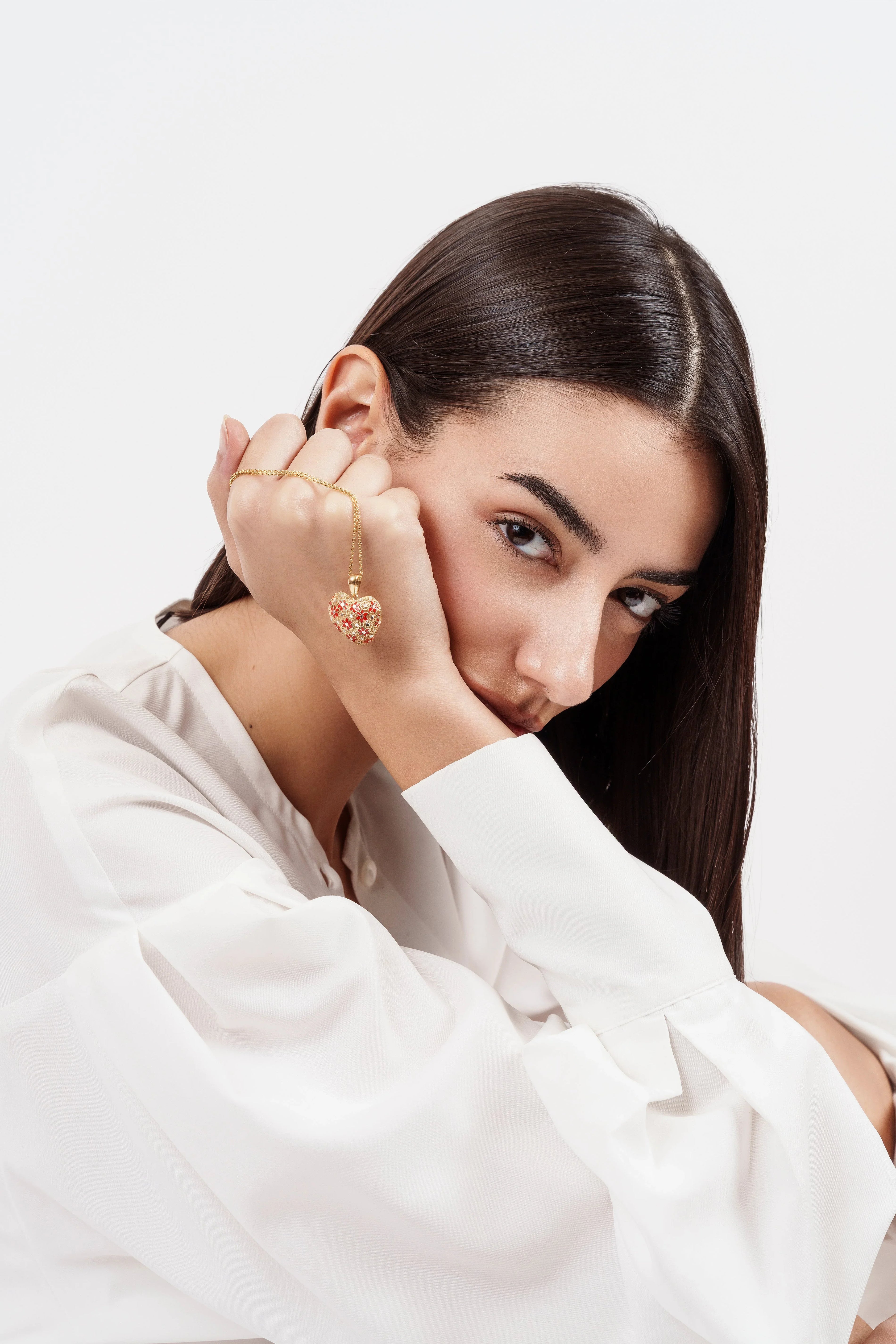 Woman in white blouse holding gold heart-shaped pendant necklace with red gems