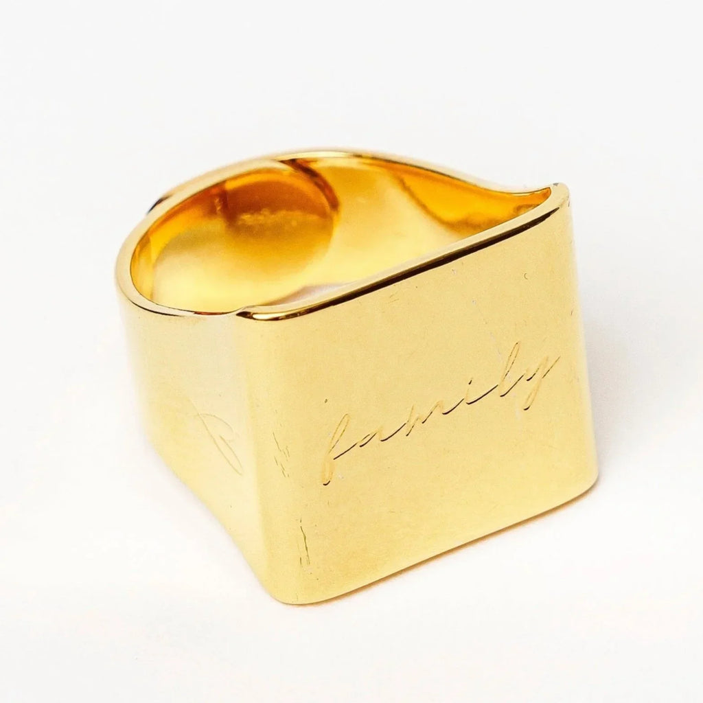 Gold signet ring with engraved cursive word "family" on flat surface