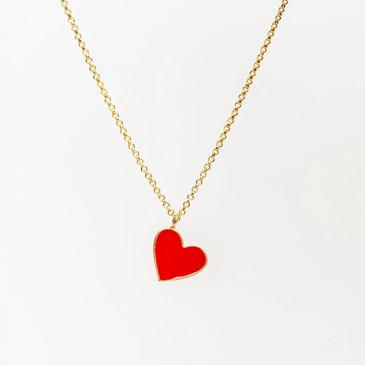 Gold chain necklace with shiny red heart-shaped pendant on white background