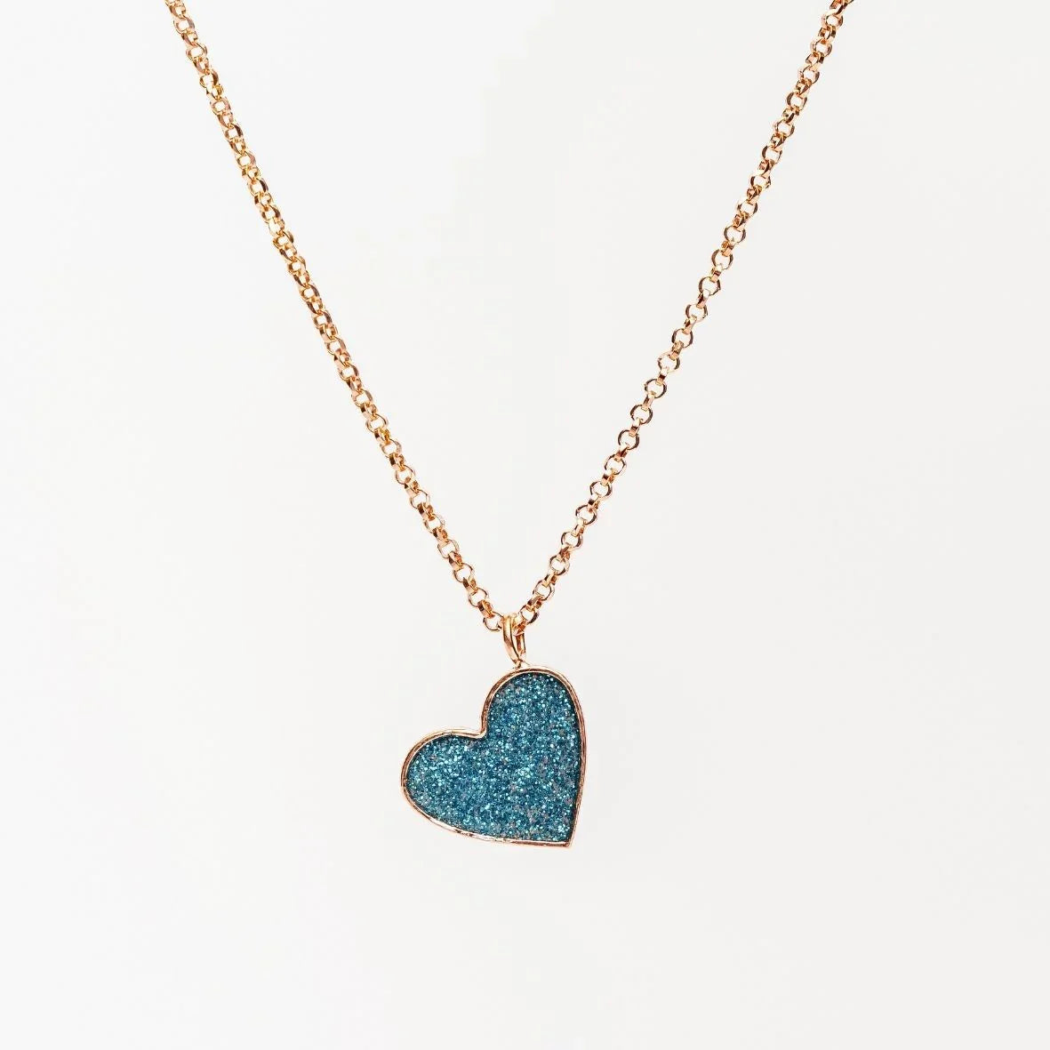 Gold chain necklace with a sparkling blue heart-shaped pendant on white background