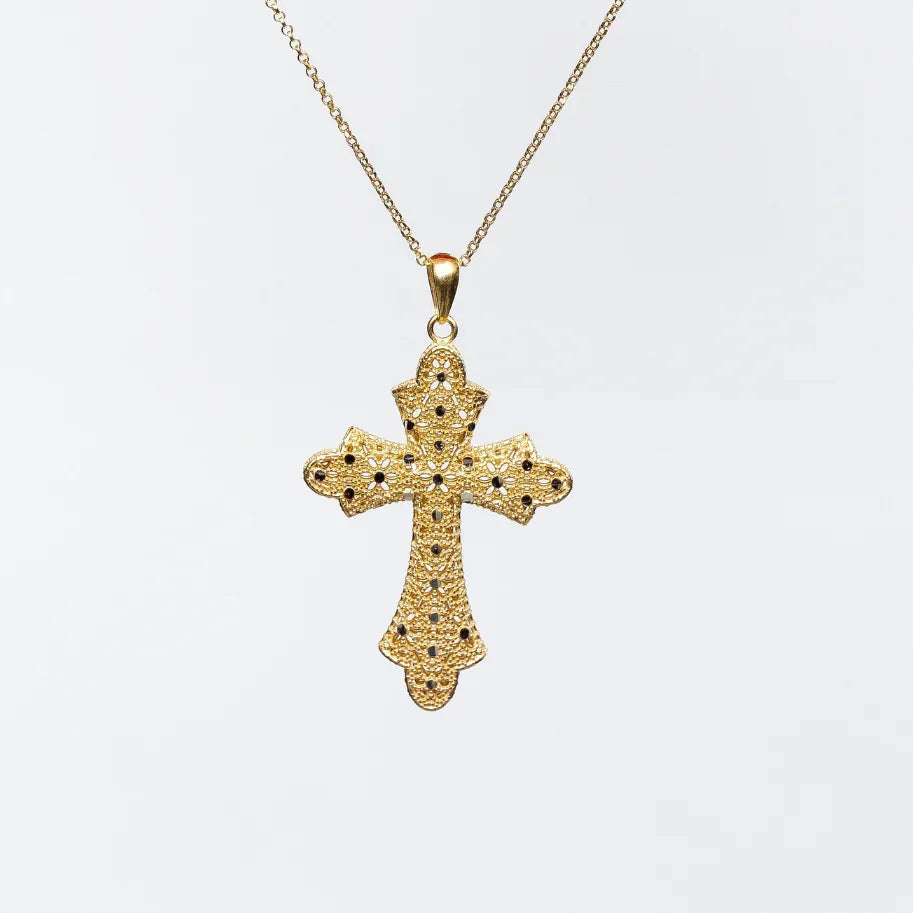Elegant gold cross pendant necklace with intricate filigree and black gemstone accents on white background