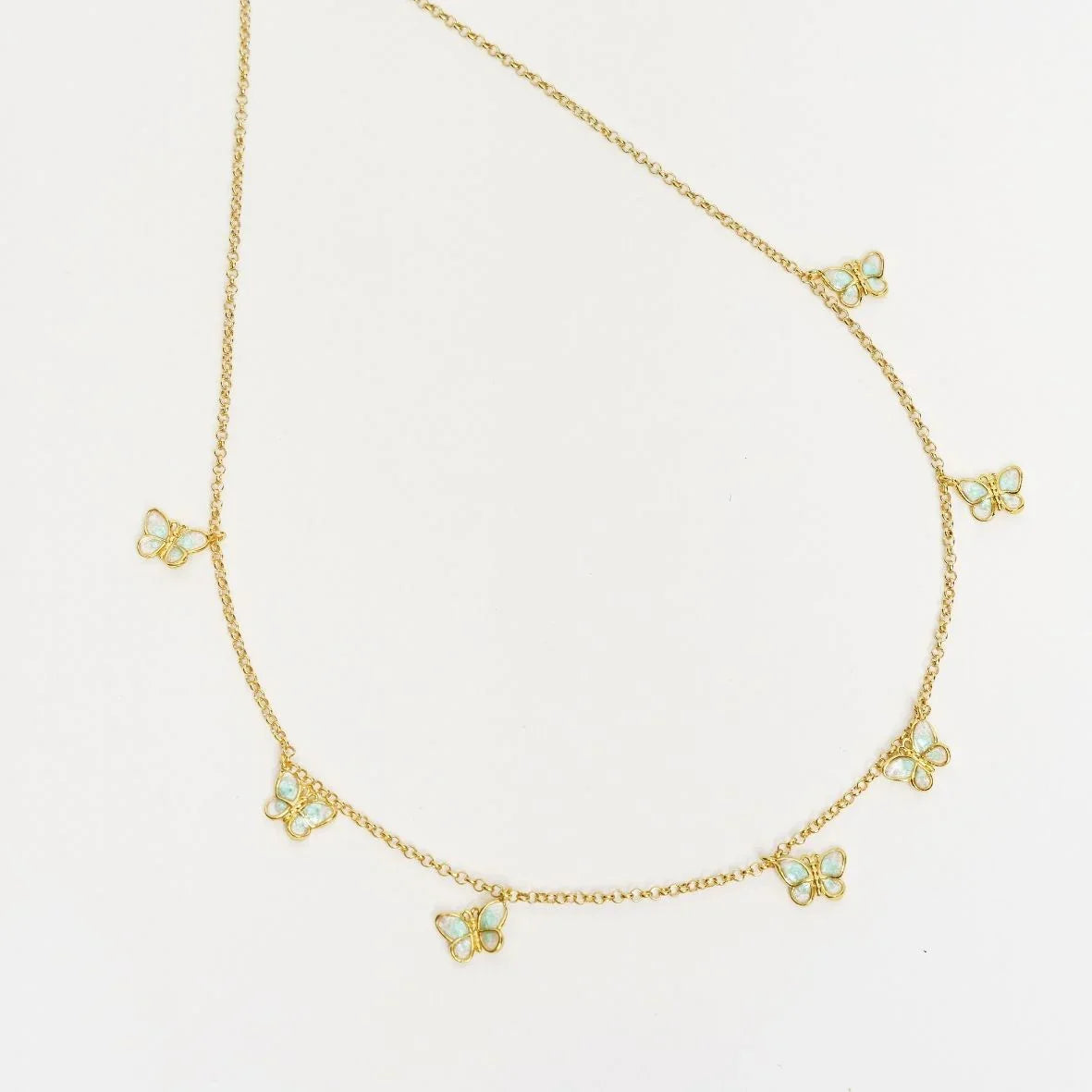 Gold chain necklace with small blue opal butterfly charms on white background