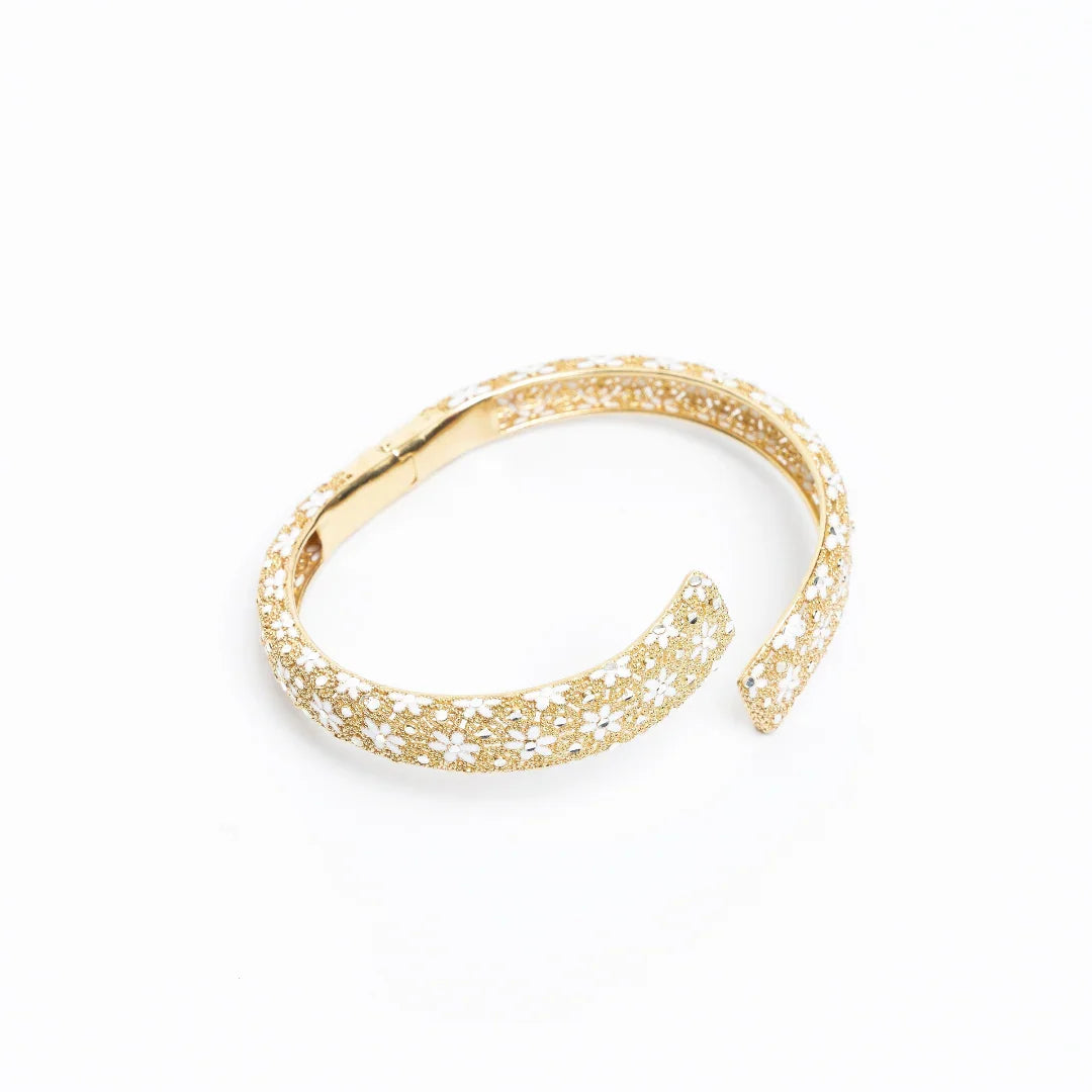 Elegant gold bangle bracelet with intricate floral white enamel design on white background