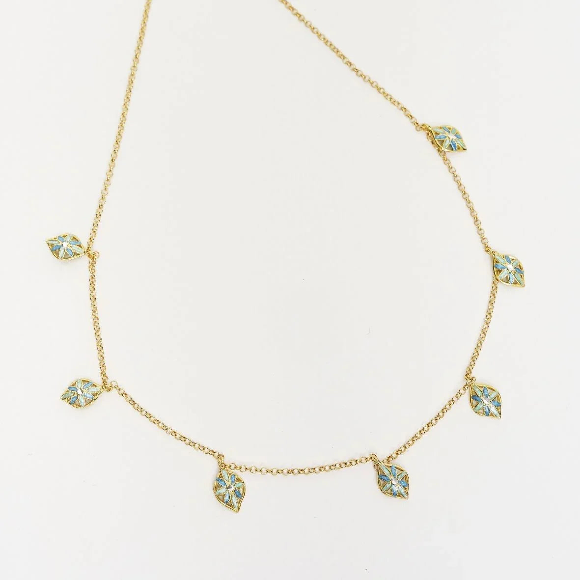 Delicate gold chain necklace with blue floral leaf charms on white background