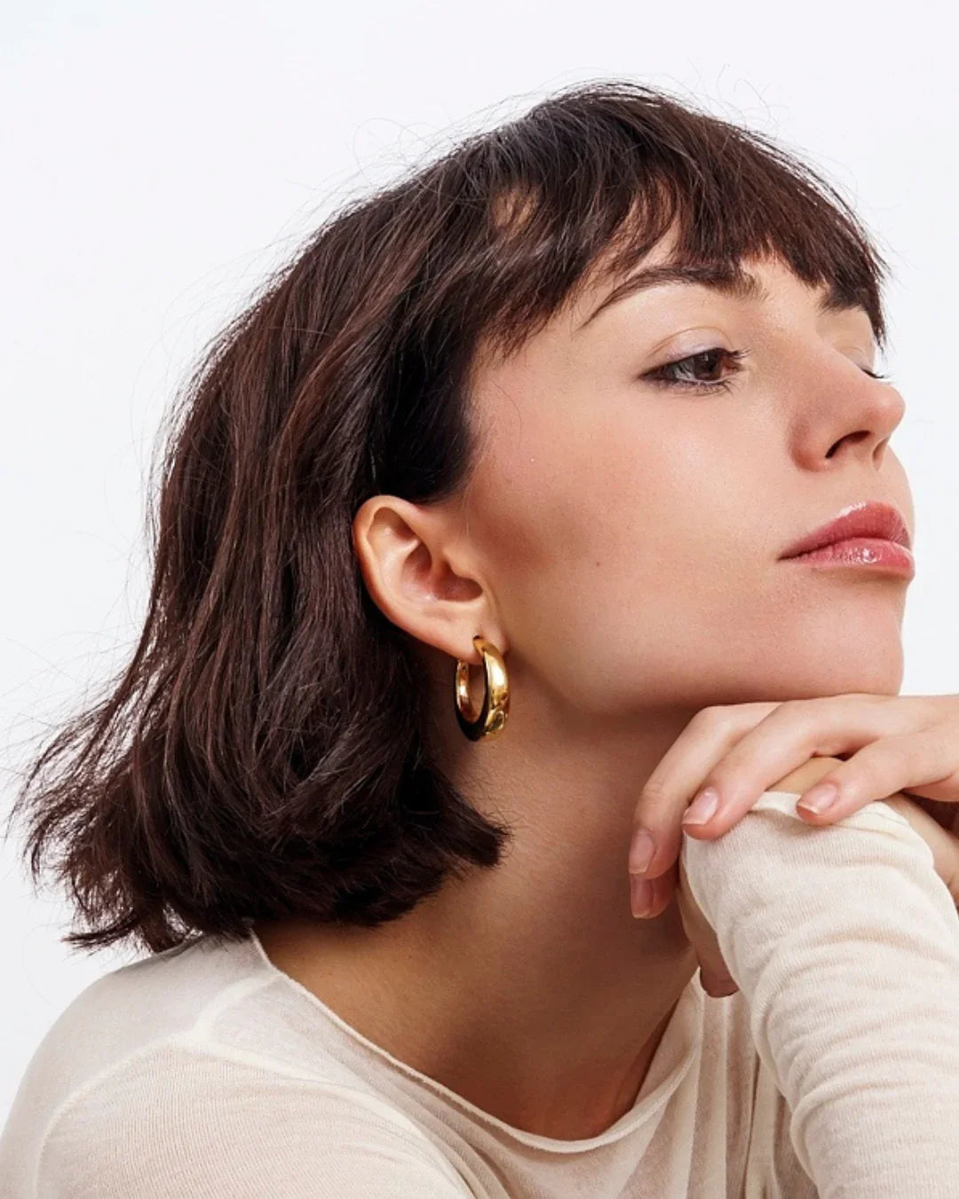 Close-up of woman with short dark hair wearing gold hoop earrings and a white top