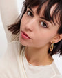 Close-up of woman with dark hair wearing gold hoop earrings and a cream top
