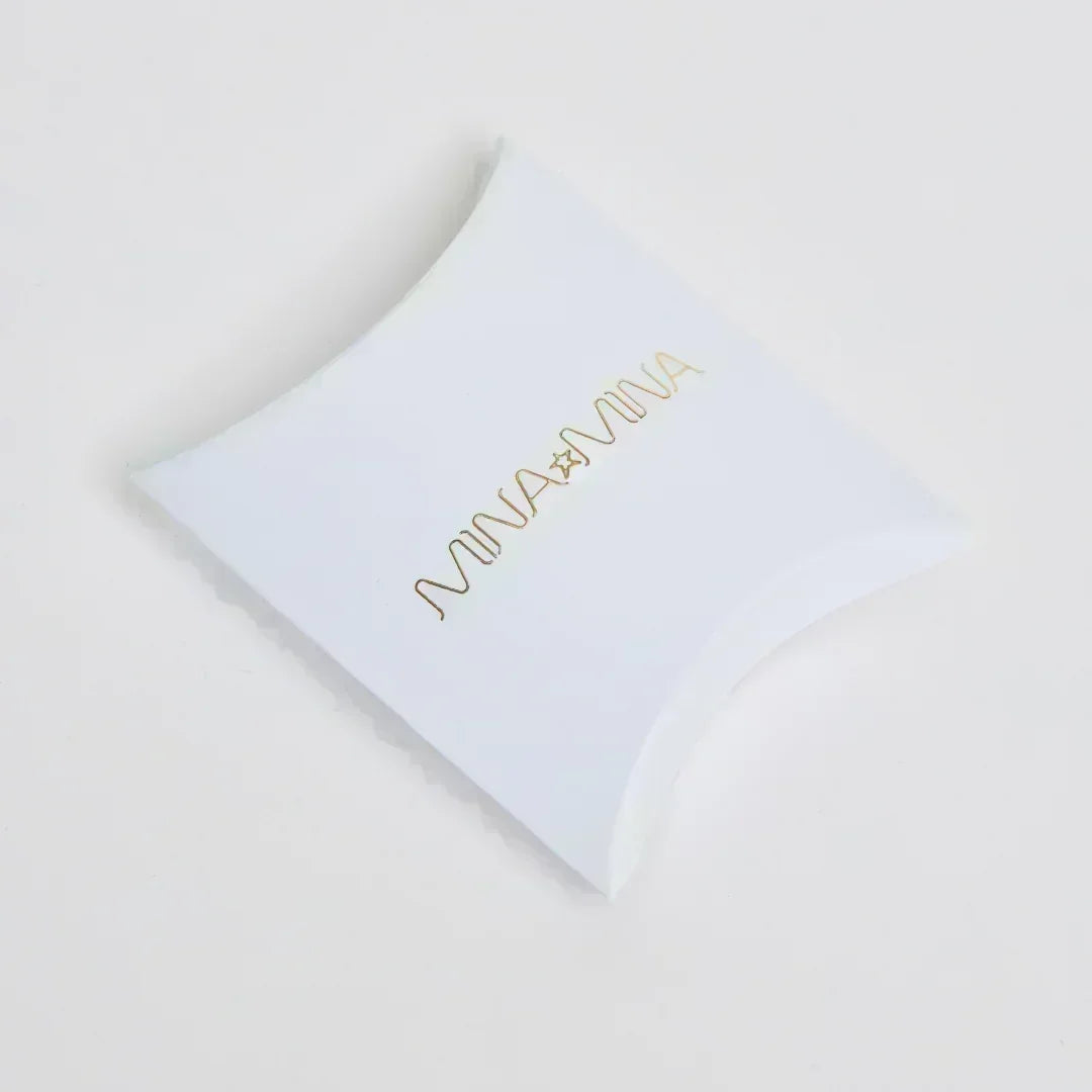 White pillow box packaging with MINA gold foil logo on plain white background