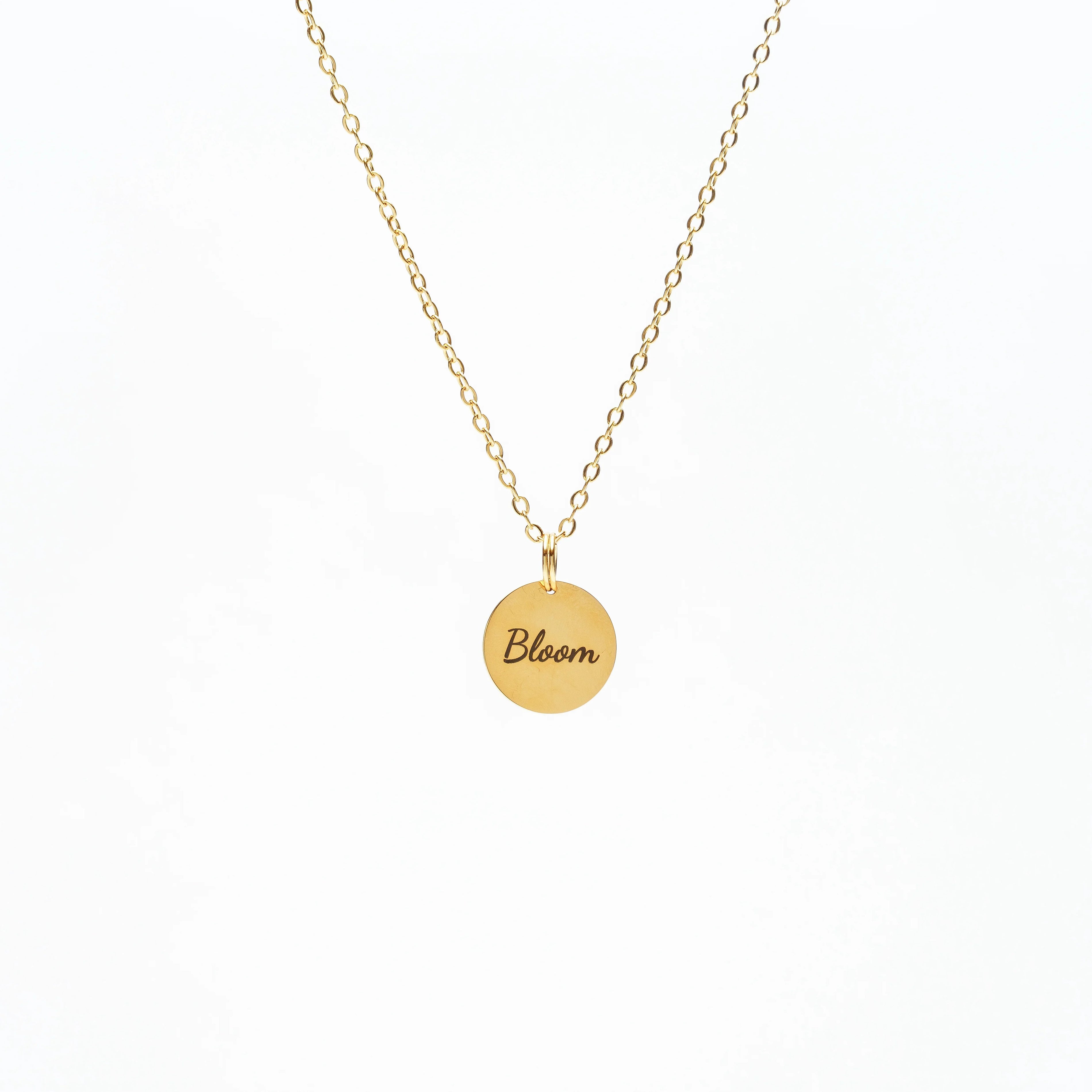 Gold chain necklace with round pendant engraved 'Bloom' on white background
