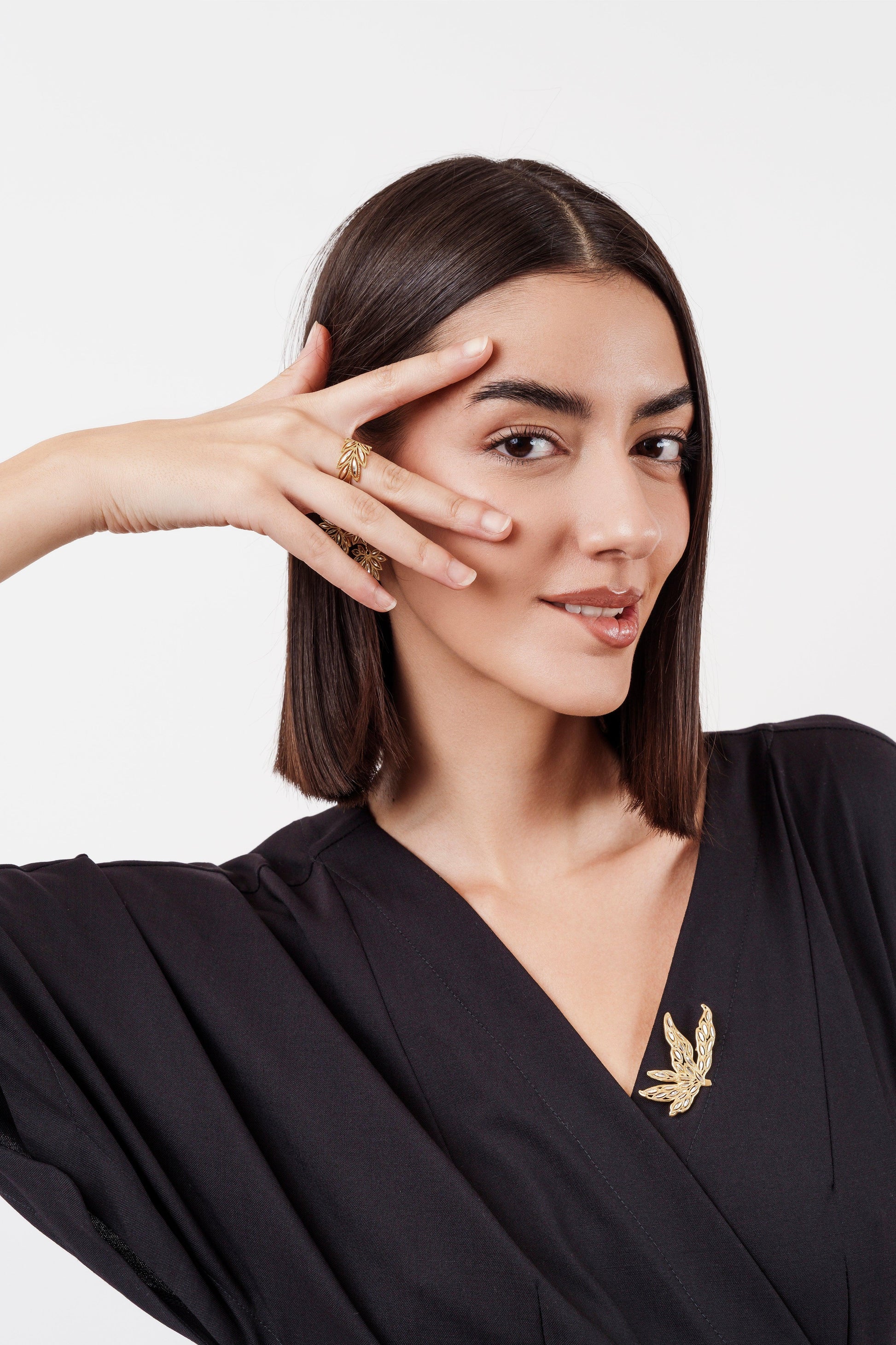 Woman wearing black dress with gold leaf brooch and matching gold leaf rings posing against white background