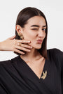 Woman in black top wearing gold floral earrings, matching ring, and leaf-shaped brooch, winking