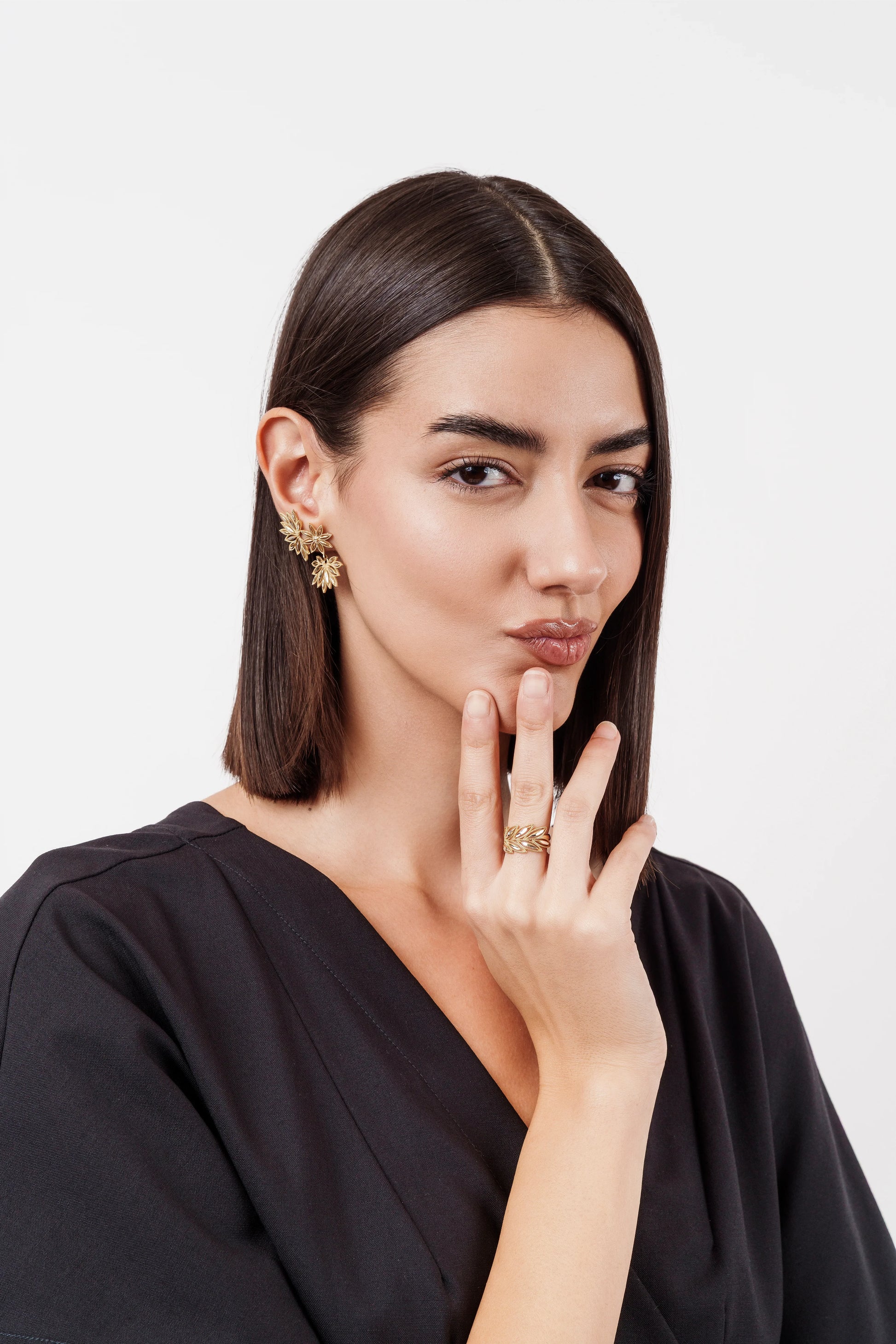 Woman with straight dark hair wearing black top, gold leaf earrings, and a matching gold leaf ring