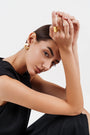 Portrait of woman in black dress wearing gold hoop earrings and wide gold ring against white background