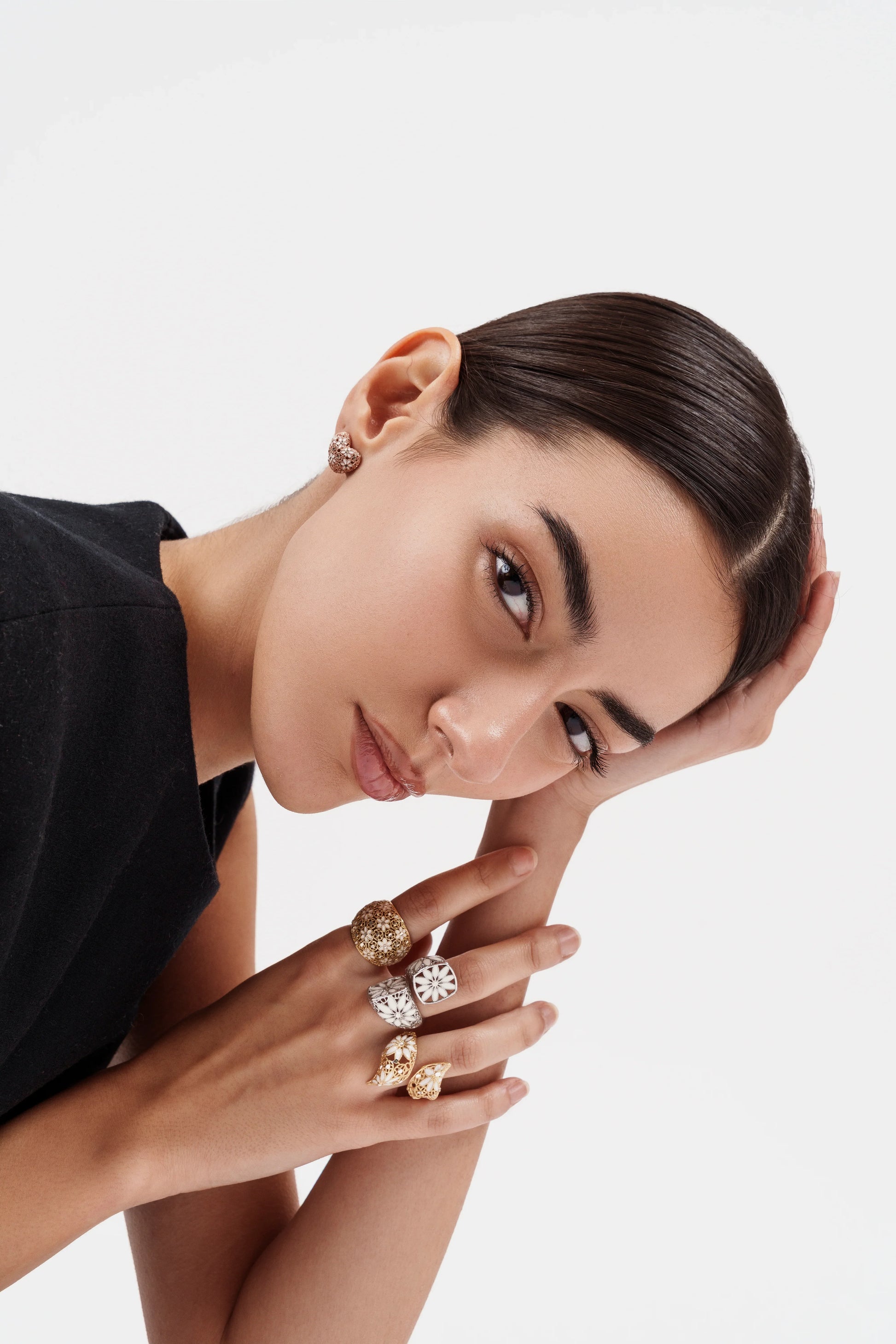 Woman with sleek hair wearing gold and white floral rings and a gold earring against white background