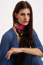 Woman with long dark hair wearing pleated blue dress, colorful patterned neck scarf, and star-shaped earrings