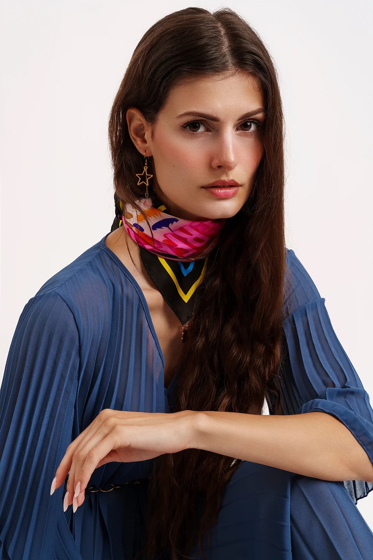 Woman with long dark hair wearing pleated blue dress, colorful patterned neck scarf, and star-shaped earrings