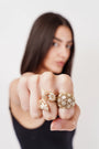Close-up of hand with three ornate gold and white floral rings, woman blurred in background