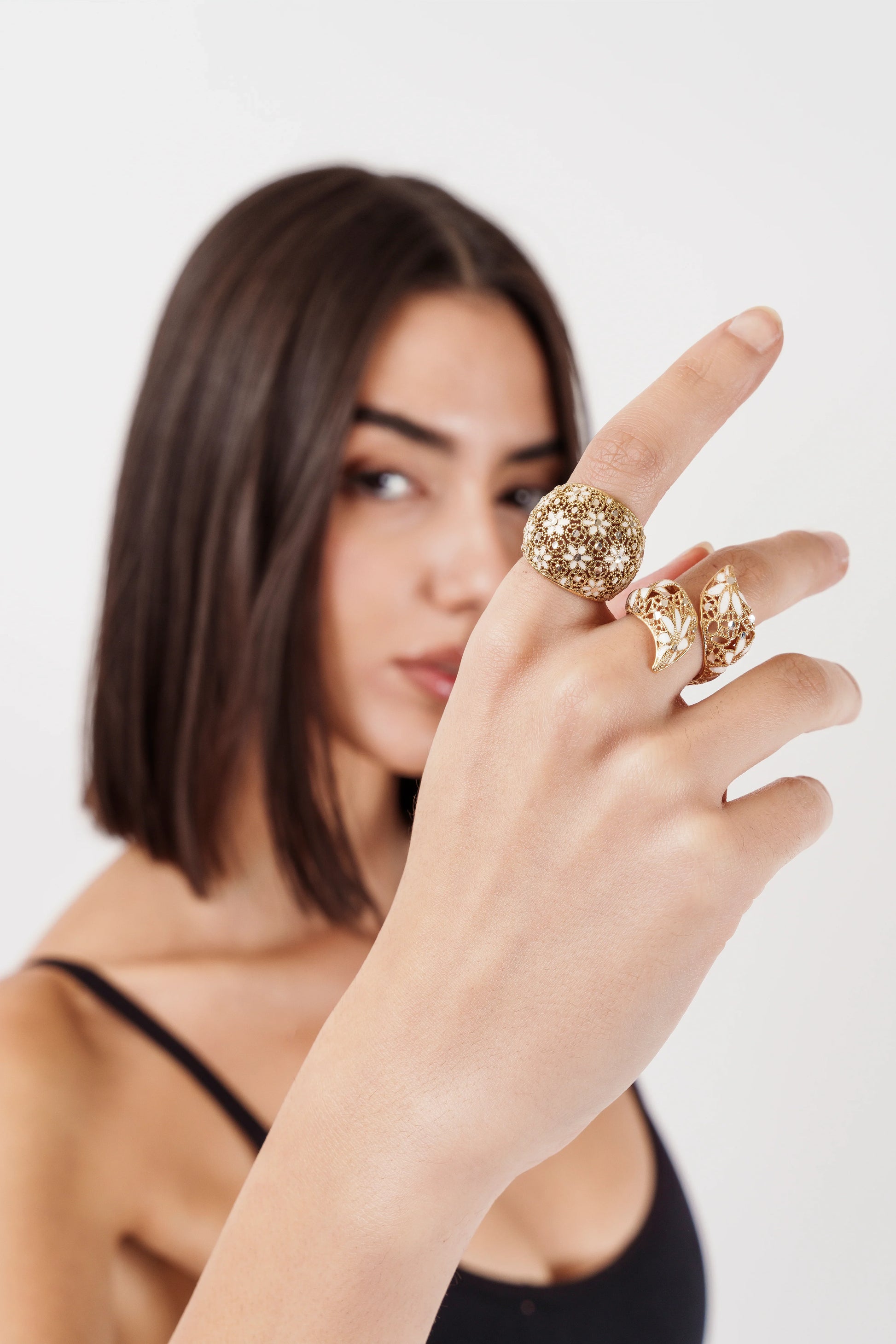 Woman with shoulder-length brown hair wearing three ornate gold rings on her fingers against white background