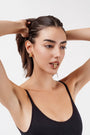 Woman in black tank top posing with gold abstract earrings and matching gold ring held between her lips